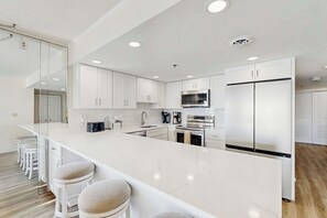 A modern kitchen with white cabinetry, a large island with bar stools, stainless steel appliances, and recessed ceiling lighting. - Plaza 701 (Ocean City)