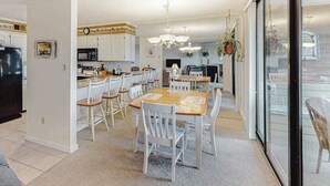 Une cuisine moderne avec des meubles blancs, un coin repas avec des chaises blanches et une grande fenêtre.