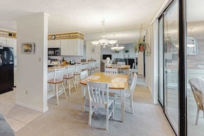 A modern kitchen with white cabinets, a dining area with white chairs, and a large window. - Convenient Coastal Condo w/Shared Outdoor Pool, Private Washer/Dryer, Free WiFi (Ocean City)