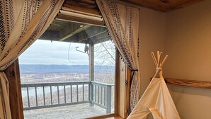 Een kamer met een groot raam, een houten vloer, een rond tapijt met een patroon en een witte tipi.