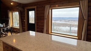 Een keuken met een groot eiland, houten kastjes en zicht op een besneeerd landschap door de ramen.