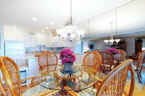 A dining area with a round glass table, wicker chairs, and a chandelier. - Our Place At The Beach 106C (Ocean City)