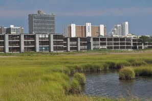 A modern building complex with multiple floors, a flat roof, and a river in the foreground. - Our Place At The Beach 106C (Ocean City)