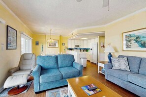 A living room with a sofa, a recliner, a coffee table, and a kitchen in the background. - Ocean Block Condo w/ 2 Balconies, AC, Fireplace, Laundry & Shared Pool (Ocean City)