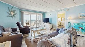 A living room with a sofa, armchair, coffee table, TV, and a painting. - Airy Beachfront Condo w/Great Views, Private Balcony, W/D, Shared Outdoor Pool (Ocean City)