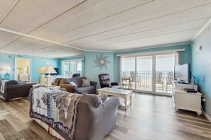 Ein geräumiges Wohnzimmer mit einem großen Fenster, einem Flachbildfernseher und einem Balkon mit Sitzgelegenheiten.