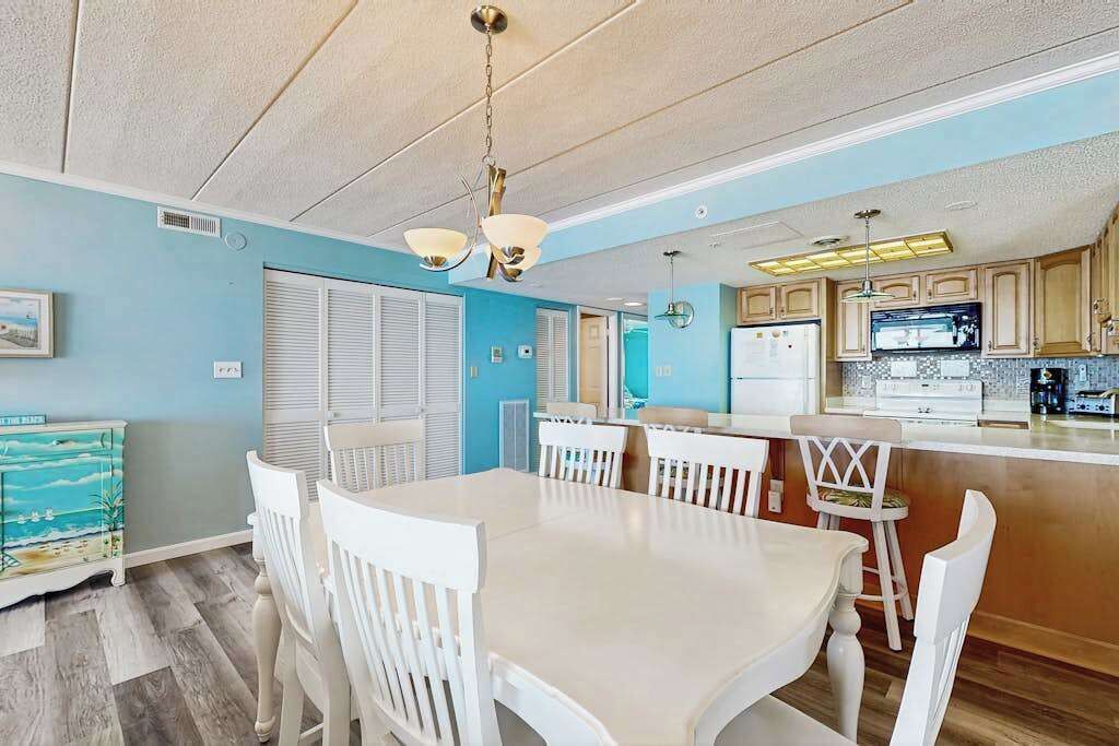 A dining area with a white table and chairs, a kitchen with wooden cabinets, and a blue wall.