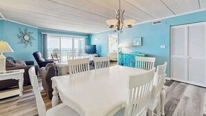 A spacious living room with a white dining table, blue walls, and a large window. - Airy Beachfront Condo w/Great Views, Private Balcony, W/D, Shared Outdoor Pool (Ocean City)