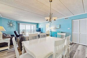 Ein geräumiges Wohnzimmer mit Esstisch in Weiß, blauen Wänden und einem großen Fenster.