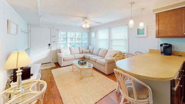 A living room with a sofa, coffee table, and chairs, a kitchen area with a counter and cabinets, and a ceiling fan. - Top-Floor Condo w/ Shared Deck, Central AC, Washer/Dryer - 1 Block to Beach (Ocean City)