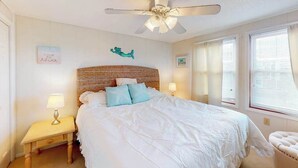 A bedroom with a bed, a nightstand, a ceiling fan, a wall-mounted decoration, and a window with blinds. - Top-Floor Condo w/ Shared Deck, Central AC, Washer/Dryer - 1 Block to Beach (Ocean City)