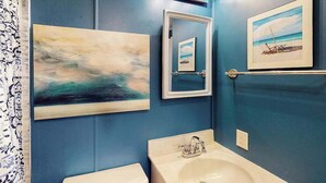 A bathroom with a blue wall, a sink, a mirror, and a painting of a beach scene. - Top-Floor Condo w/ Shared Deck, Central AC, Washer/Dryer - 1 Block to Beach (Ocean City)