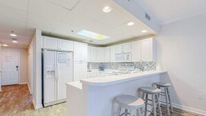 A modern kitchen with white cabinetry, a central island with stools, and a microwave above the sink. - Newly Updated Condo Steps from the Beach w/ Balcony, Shared Rooftop Pool (Ocean City)
