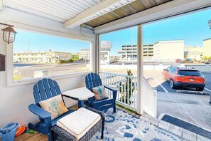 Un espace extérieur aménagé, abrité, avec deux chaises bleues et une table, d’où l’on a vue sur un parking et des bâtiments.