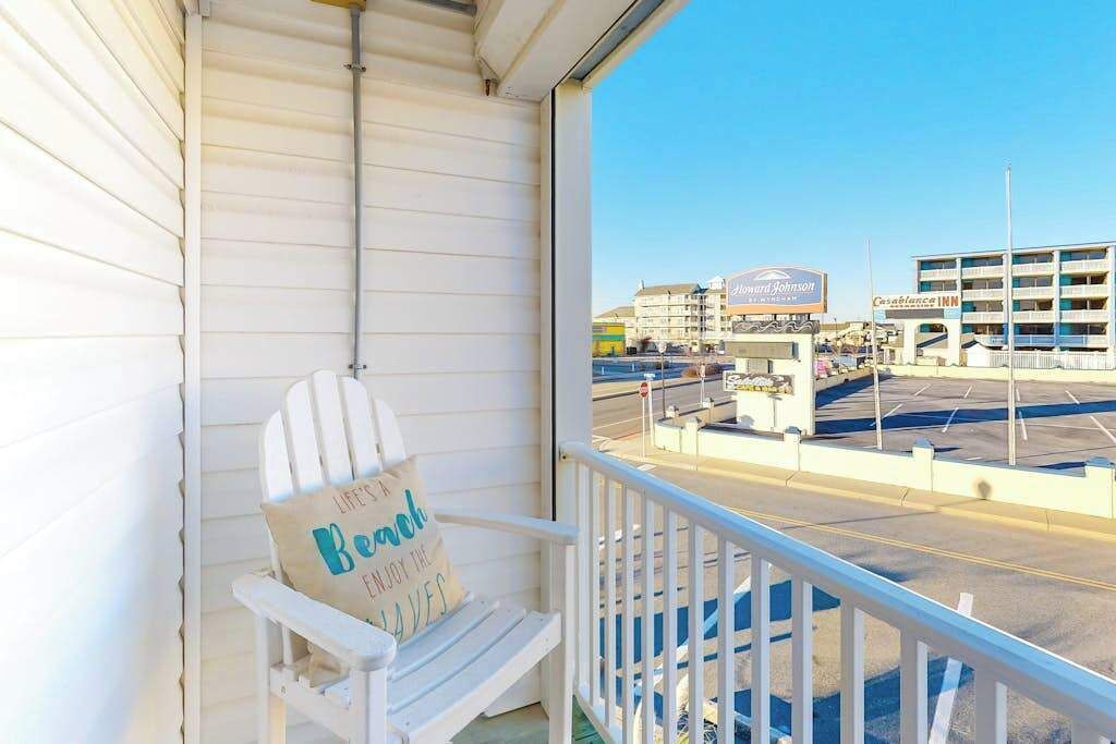 Une chaise blanche avec un coussin, placée sur un balcon, d’où l  ’on aperçoit un parking et des immeubles.