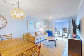 Ein Wohnzimmer mit einem Holzesstisch, einer Couch, einem blauen Sessel, einer Lampe und einem Fernseher auf einem Schrank.