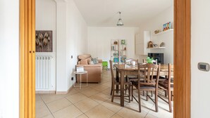 Una sala de estar con sofá, una mesa de comedor con sillas, un radiador y una estantería.
