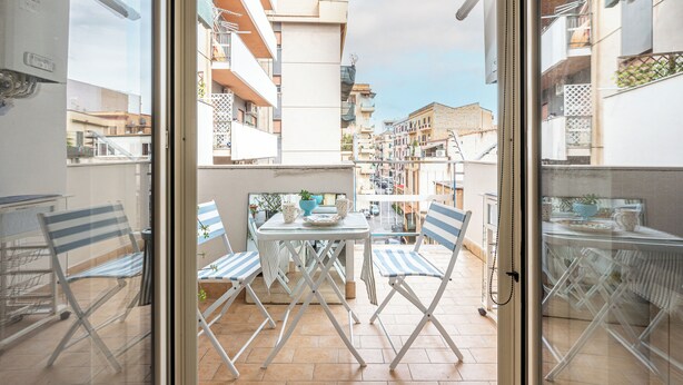 Un balcón con mesa y sillas, vistas de la ciudad y un edificio con balcones.