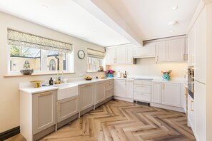 Une cuisine moderne avec des meubles blancs, un parquet en bois disposé en chevrons et une fenêtre donnant sur l’extérieur.