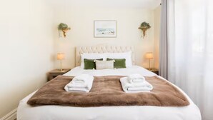Camera d'albergo con un letto, due comodini, una testiera, una finestra con tende e piante sospese al muro.
