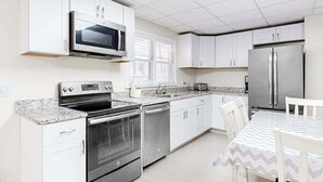 A kitchen with white cabinets, stainless steel appliances, a microwave, oven, dishwasher, and a table with chairs. - Gorgeous & roomy condo with partial AC & full kitchen - steps from beach access (Ocean City)
