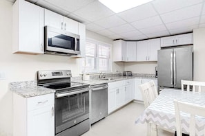 A kitchen with white cabinets, stainless steel appliances, a microwave, oven, dishwasher, and a table with chairs. - Gorgeous & roomy condo with partial AC & full kitchen - steps from beach access (Ocean City)