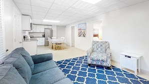A modern living room with a blue patterned rug, a gray sofa, a patterned armchair, and a small white side table. - Gorgeous & roomy condo with partial AC & full kitchen - steps from beach access (Ocean City)