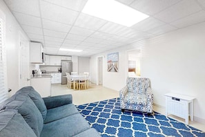 A modern living room with a blue patterned rug, a gray sofa, a patterned armchair, and a small white side table. - Gorgeous & roomy condo with partial AC & full kitchen - steps from beach access (Ocean City)