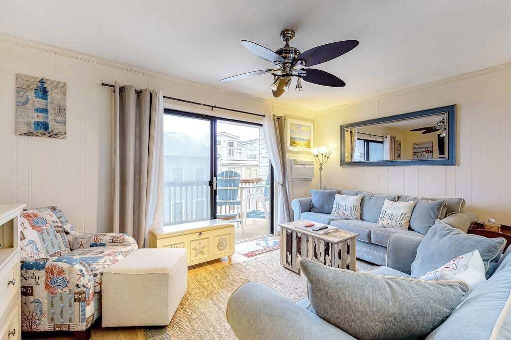 Una sala de estar con sofá, reposapiés y ventilador de techo.