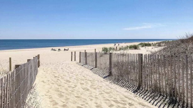 Een zandstrand met een houten omheining die naar het water leidt.