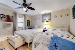 Ein Zimmer mit zwei Betten, einem Deckenventilator, einer Flagge, einem Strandbild und einem nautisch inspirierten Kissen.
