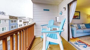 Een balkon met houten hekwerk, een blauw-witte stoel en een blauwe bank in een kamer met uitzicht op omliggende gebouwen.