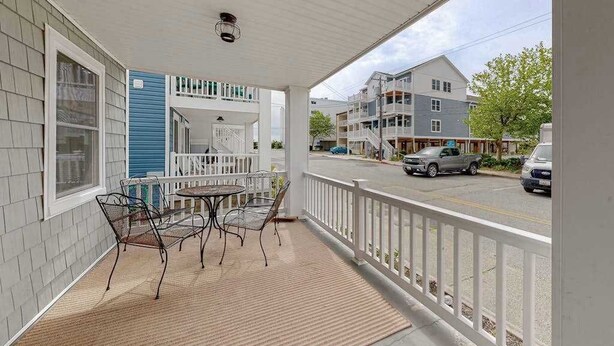 A covered porch with a table and chairs, a white railing, and a view of a street with cars and buildings. - Newly remodeled, ocean block condo with balcony, central AC & W/D (Ocean City)