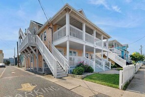 Ein zweistöckiges Gebäude mit einem Balkon im zweiten Stock, einer Treppe, die zum Eingang führt, und einem Parkschild in der Straße.