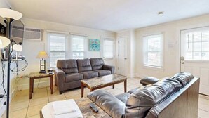 A living room with a sofa, a coffee table, and a lamp. There is a door and windows with blinds. - Casa Sophia #12 (Ocean City)