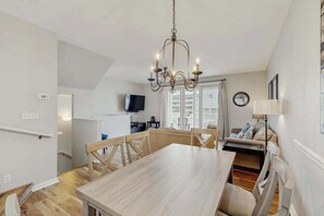 A dining area with a wooden table and chairs, a chandelier, a television in the background, and a view of the outside. - Newly Renovated, 3-Story Townhome with Balconies, WiFi, AC & Washer/Dryer (Ocean City)