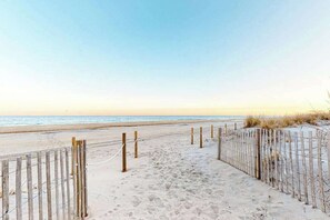 Ein Sandweg am Strand, gesäumt von Holzbefestigungen und einem Zaun, der zum Meer führt.