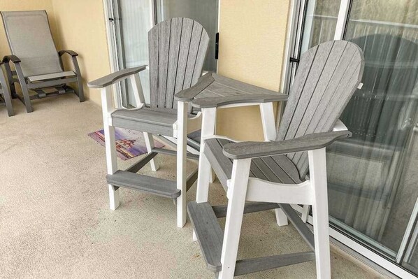 A patio area with Adirondack chairs and a small table, near a sliding glass door. - Summer House 102 (Ocean City)