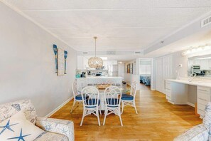 A spacious kitchen with white cabinets, a central island, and a dining area with a glass table and white chairs. - Side Ocean View Condo near the Boardwalk with Balcony, AC, WiFi & Shared Pool (Ocean City)
