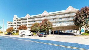 Un hotel de varios pisos con balcones, zona de estacionamiento y cielo despejado.