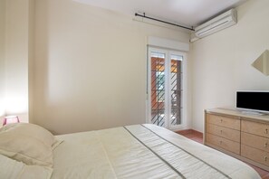 A bedroom with a bed, a dresser, an air conditioning unit, and a sliding glass door leading to an outdoor area. - Isla Canela Apartment with Shared Pool, Wi-Fi, and Air Conditioning (Ayamonte)