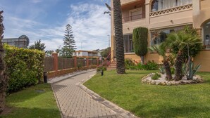 A residential building with a paved pathway, a palm tree, and a well-maintained garden.