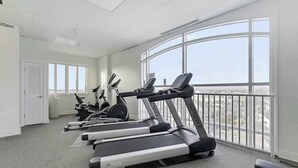 Un gimnasio con cintas de correr, elípticas y un amplio ventanal con vista a la ciudad.