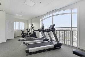 Ein Fitnessstudio mit Laufbändern, Crosstrainern und einem großen Fenster mit Blick auf die Stadt.