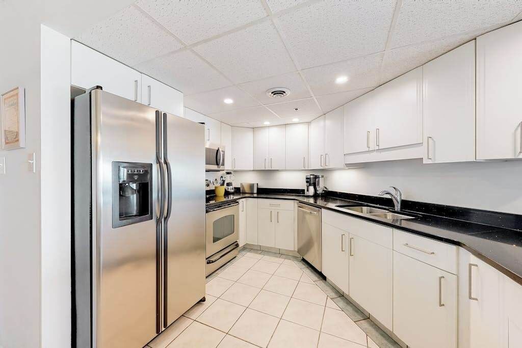 A modern kitchen with white cabinets, a stainless steel refrigerator, a microwave, and a dishwasher.