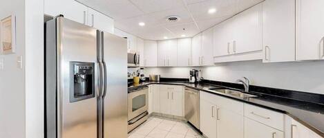 A modern kitchen with white cabinets, a stainless steel refrigerator, a microwave, and a dishwasher.