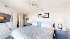 A bedroom with a bed, bedside lamps, a ceiling fan, a TV, and a framed picture on the wall. - Newly updated, oceanfront condo with balcony, views & pool (Ocean City)
