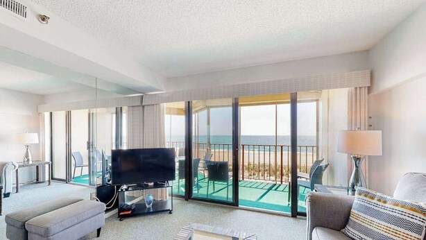 A hotel room with a balcony, a flat-screen TV, a sofa, and a coffee table. - Newly updated, oceanfront condo with balcony, views & pool (Ocean City)