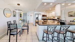 A modern kitchen with a central island, dining area with chairs, and a large mirror on the wall. - Newly updated, oceanfront condo with balcony, views & pool (Ocean City)
