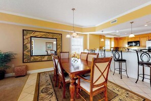 A dining area with a wooden table and chairs, a kitchen with wooden cabinets, and a large mirror on the wall. - Well-Decorated, Ocean Block Condo w/ Fireplace, Balcony & Shared Pool/Gym (Ocean City)